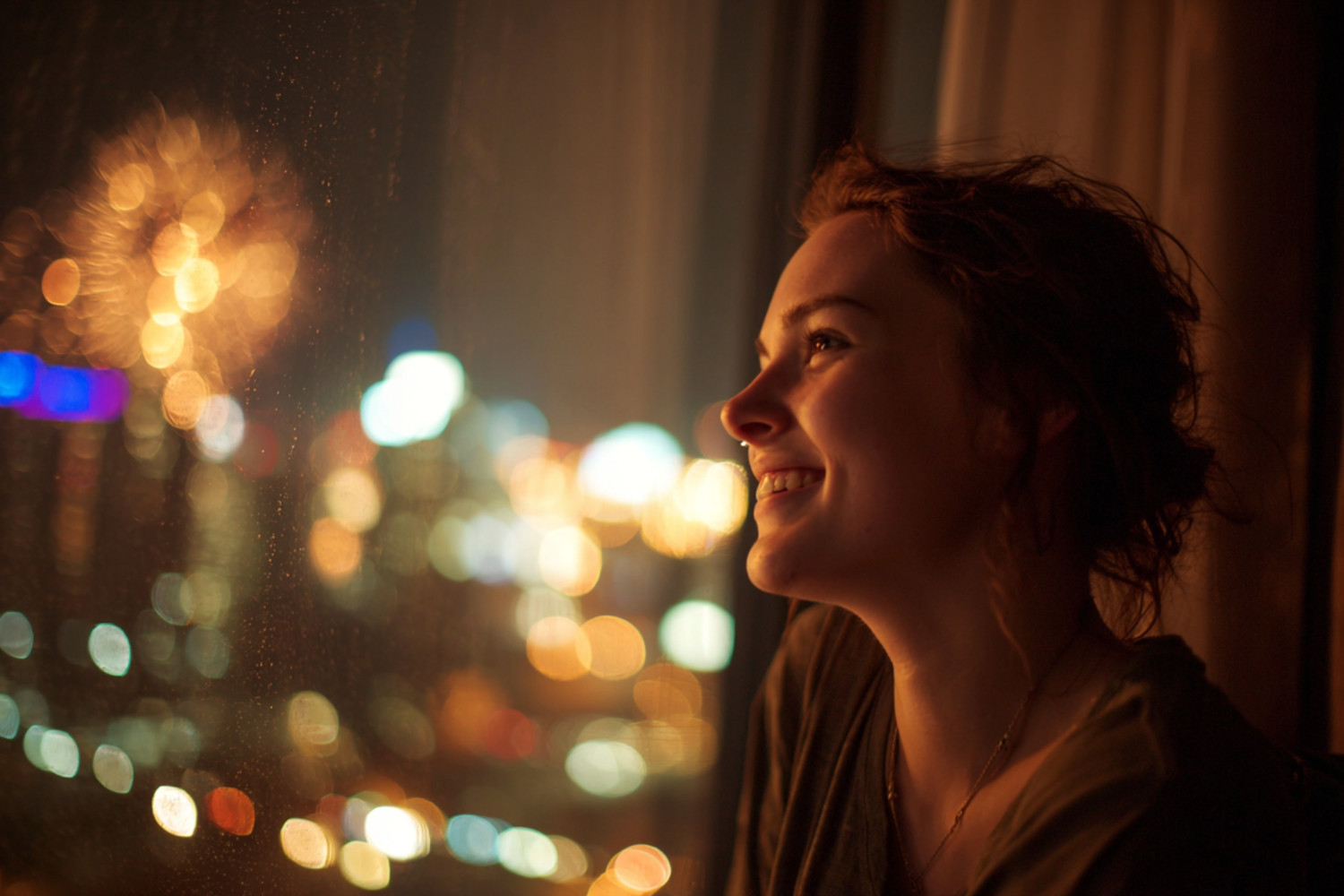 Eine Frau schaut lächelnd aus dem Fenster und beobachtet das Feuerwerk