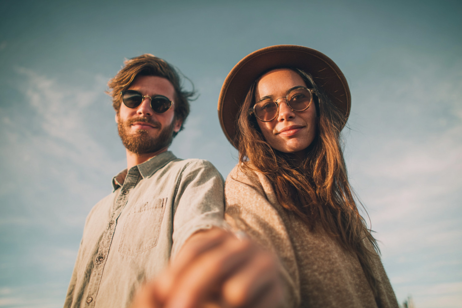 Ein  Mann und eine Frau mit Sonnenbrillen. Ihre verschränkten Hände sind in Richtung Kamera gerichtet.