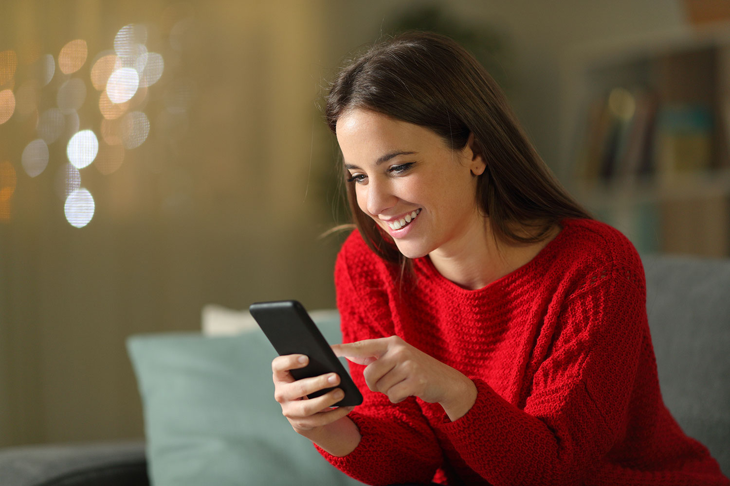 Attraktive junge Frau mit rotem Pullover in häuslicher Atmosphäre am Handy
