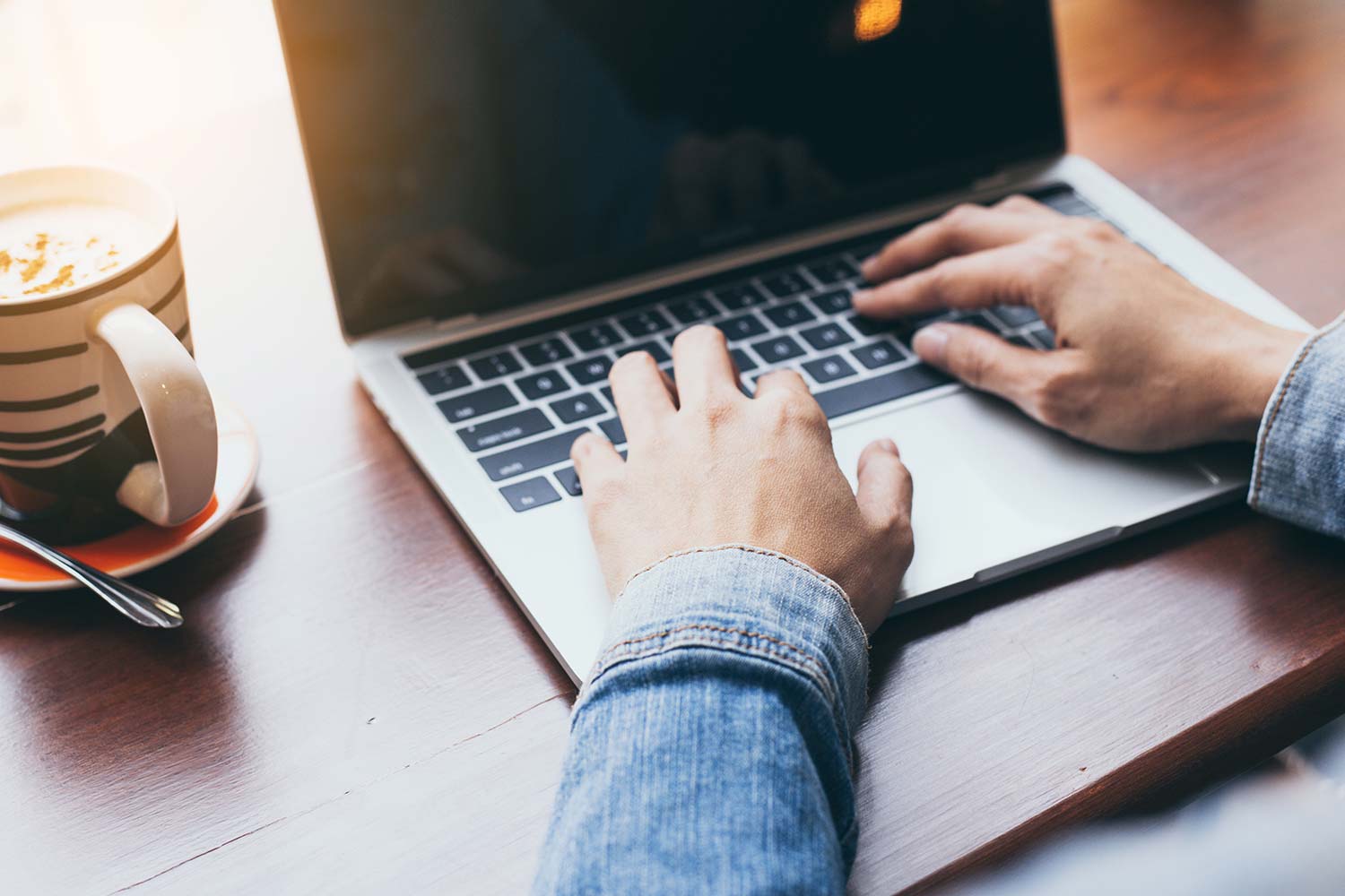 Männliche Person mit Cappuccino verwendet Laptop