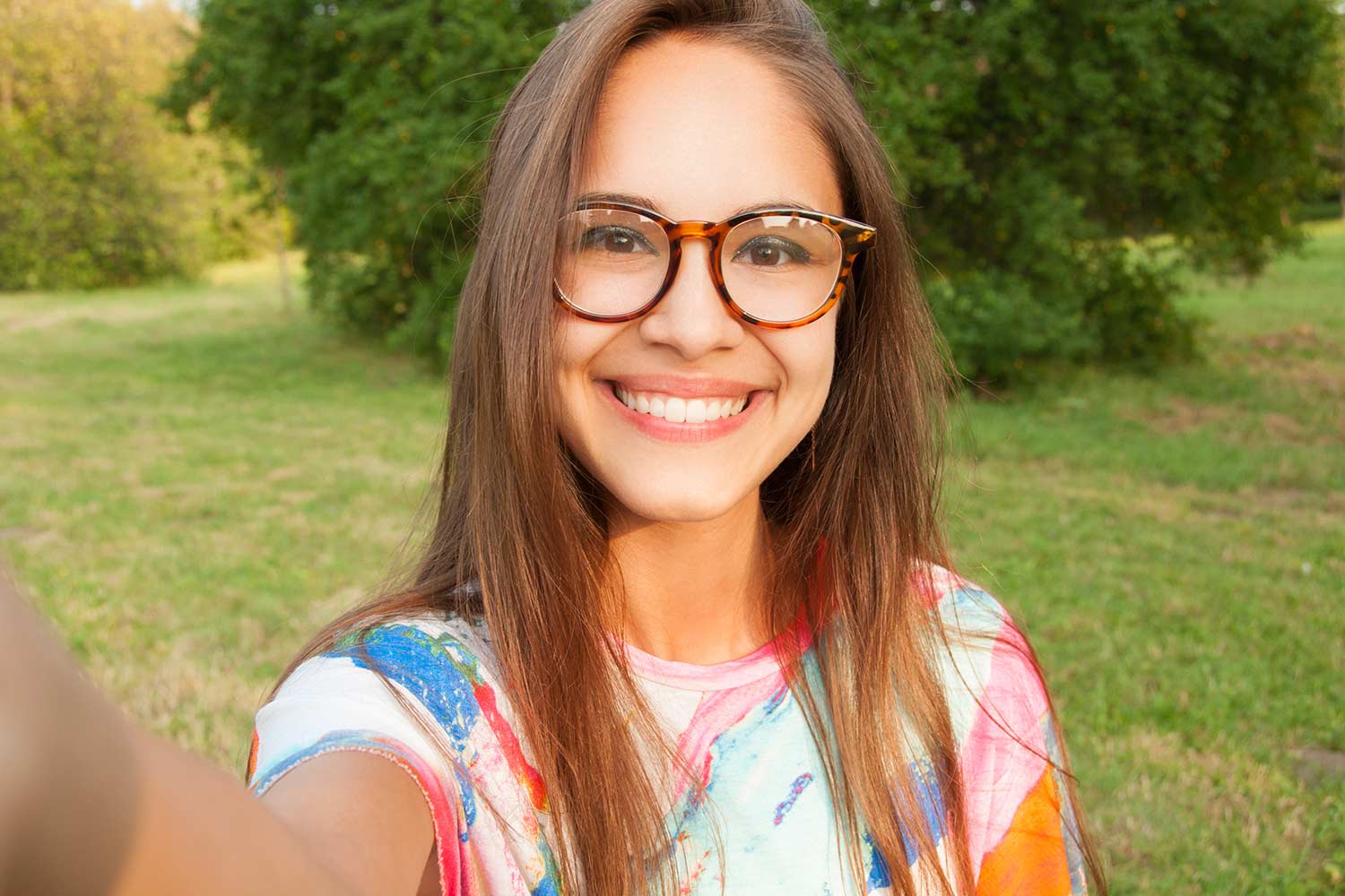 Junge lächelnde Frau mit Brille macht Selfie über ihr Smartphone